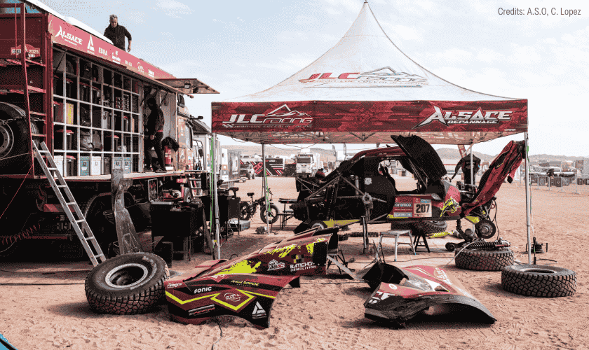 AddiDrive equipped assistance truck and race car under repair beneath a JLC Racing tent in the desert during the Dakar Rally.